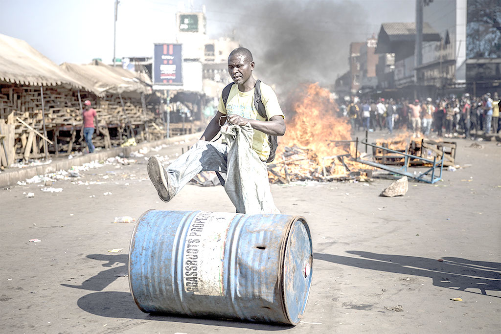 A supporter push a barrel in front of a fire  in Harare on Wedensday, as protests erupted over alleged fraud in the country's election.