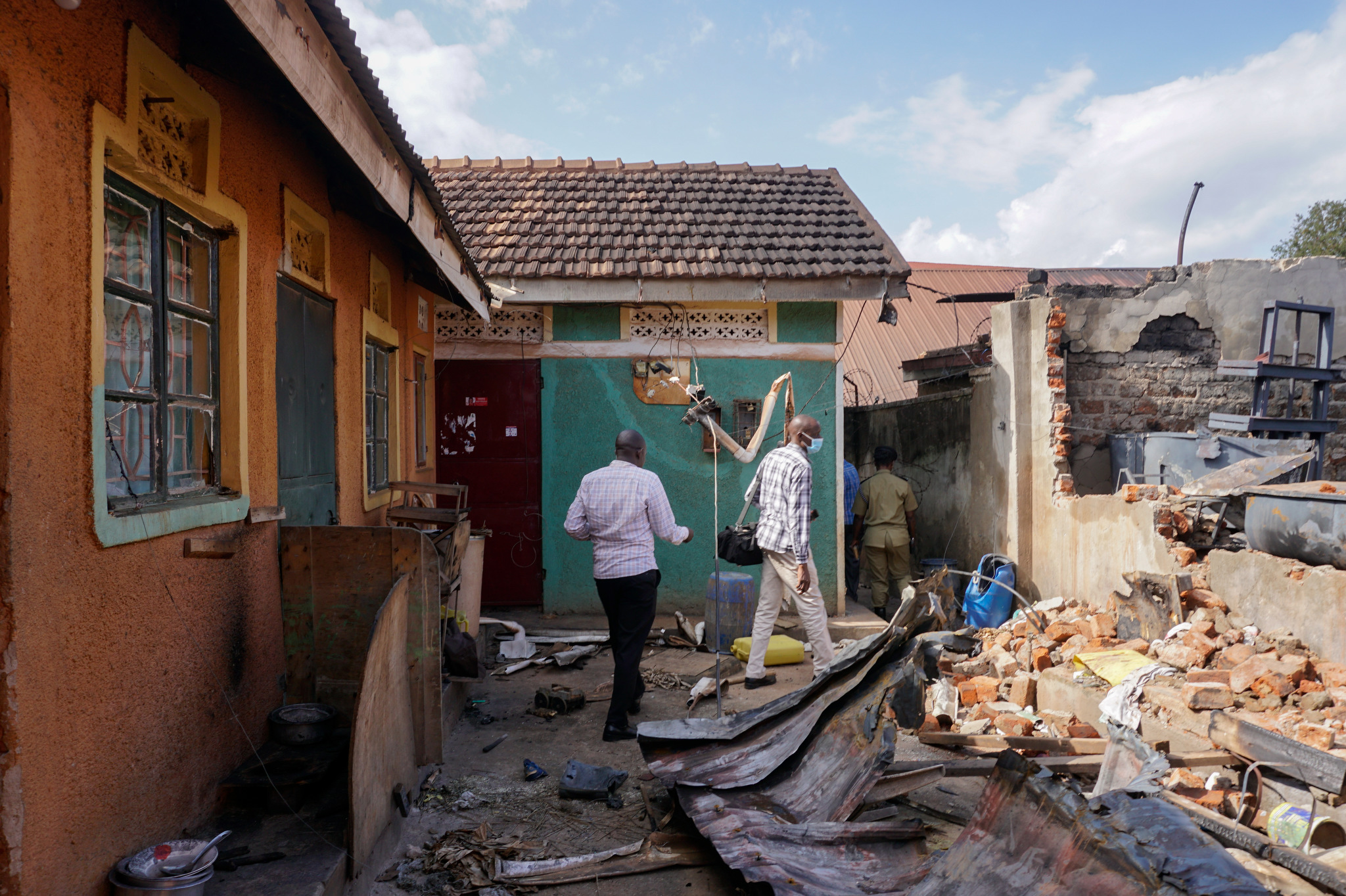 Frances Lubega (center, with bag) and his employees accompany police as they inspect damage caused by an explosion and fire at the paint factory Lubega owns. ( Photo: Edna Namara, GPJ Uganda)