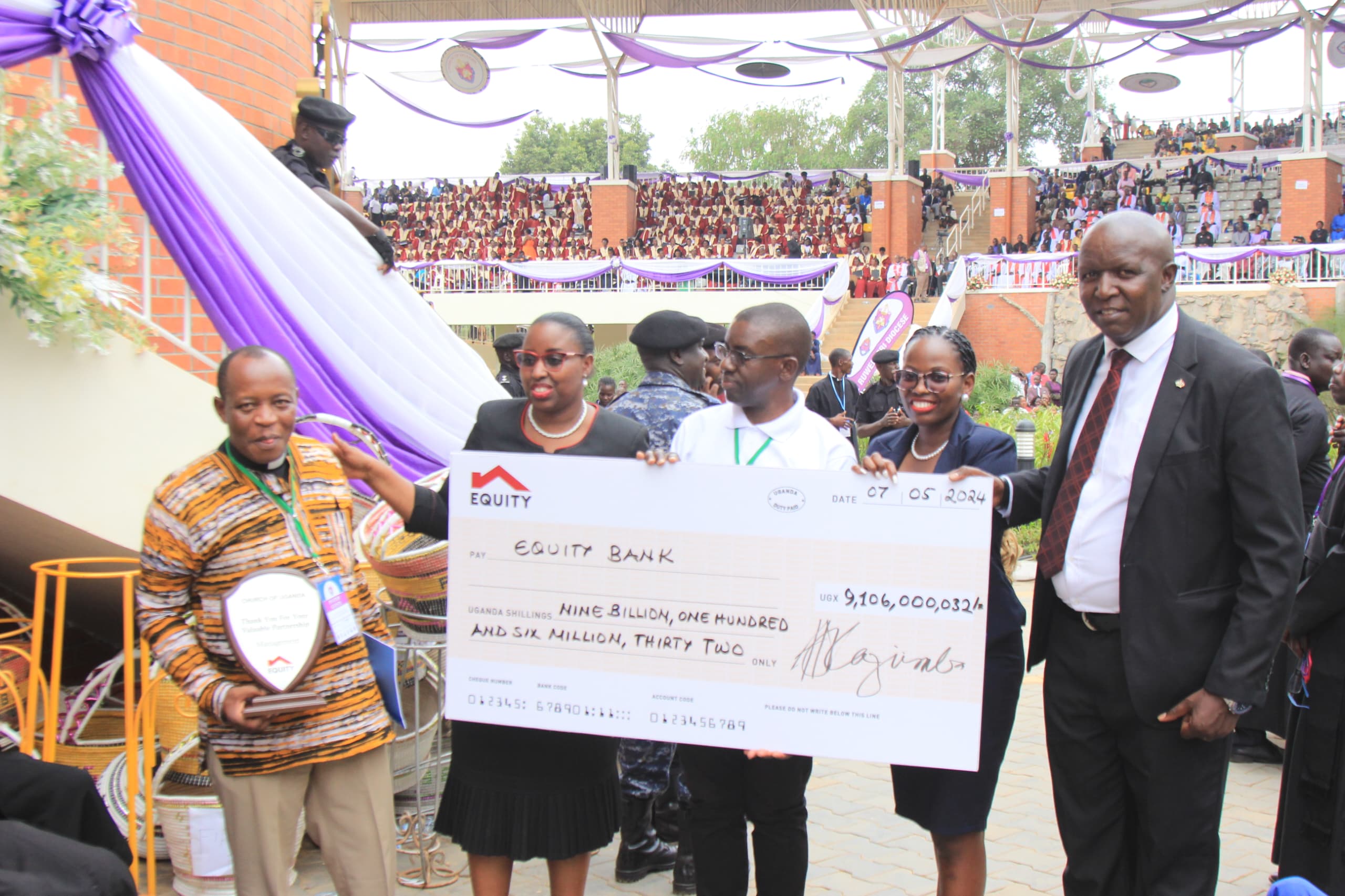 Here is a possible photo caption:"Equity Bank Executive Director Elizabeth Mwerinde Kasedde (left) presents a symbolic cheque to Archbishop Dr. Stephen Kaziimba Mugalu (right) to mark the successful repayment of the loan for the construction of Janani Luwum Church House. The ceremony took place at the Uganda Martyrs celebrations in Namugongo on Monday, June 3."