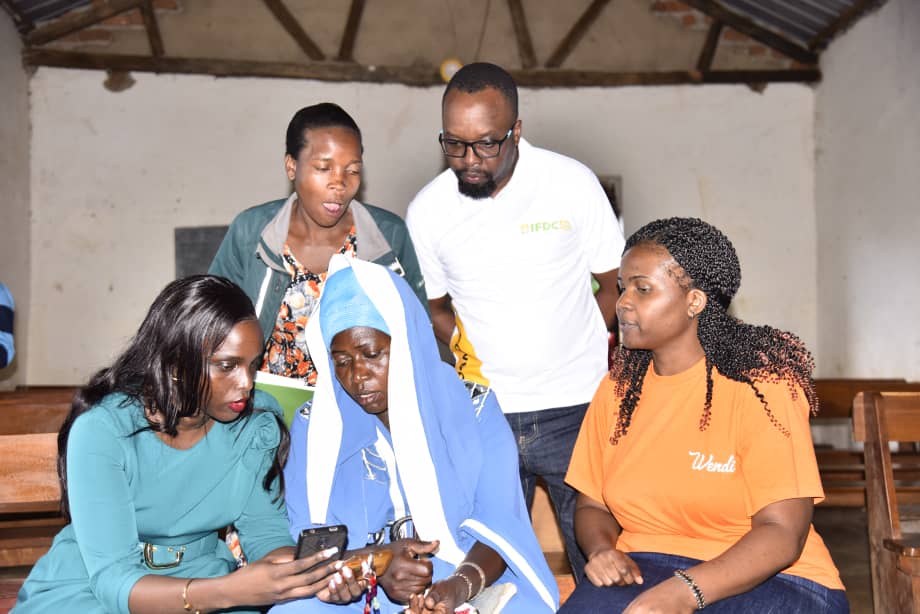 Brenda Mpoora (L), PostBank Uganda's Head of Fintech Business, demonstrates Wendi Mobile Wallet to farmers in Mbale District, alongside Roger Gilbert Nyakahuma (Center Back), IFDC BRIGHT project Financial Inclusion Manager, October 15, 2024